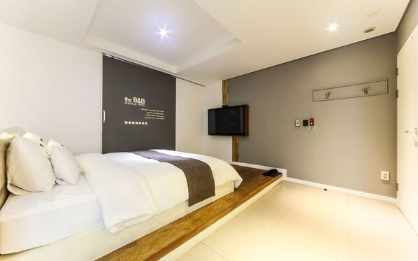 Una camera d'albergo moderna con un letto rifatto, una TV a schermo piatto montata a parete e un comodino.