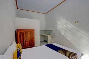 Quarto com cama, guarda-roupa de madeira, pequeno espaço de cozinha e ventoinha no teto.