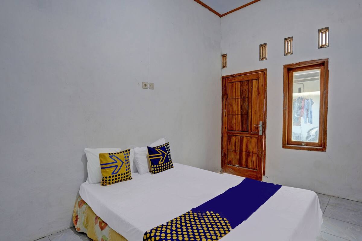 Un dormitorio con una cama, un armario de madera, un ventanal y una lámpara fijada a la pared.