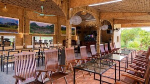 A restaurant with bamboo ceiling, wooden chairs, and tables, featuring large windows and artwork on the walls. - Tam Coc Cat Luong Homestay (Nam Hoa Lu)