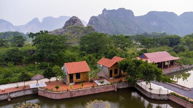 A riverside hotel with multiple buildings, a bridge, and a view of distant mountains. - Tam Coc Cat Luong Homestay (Nam Hoa Lu)