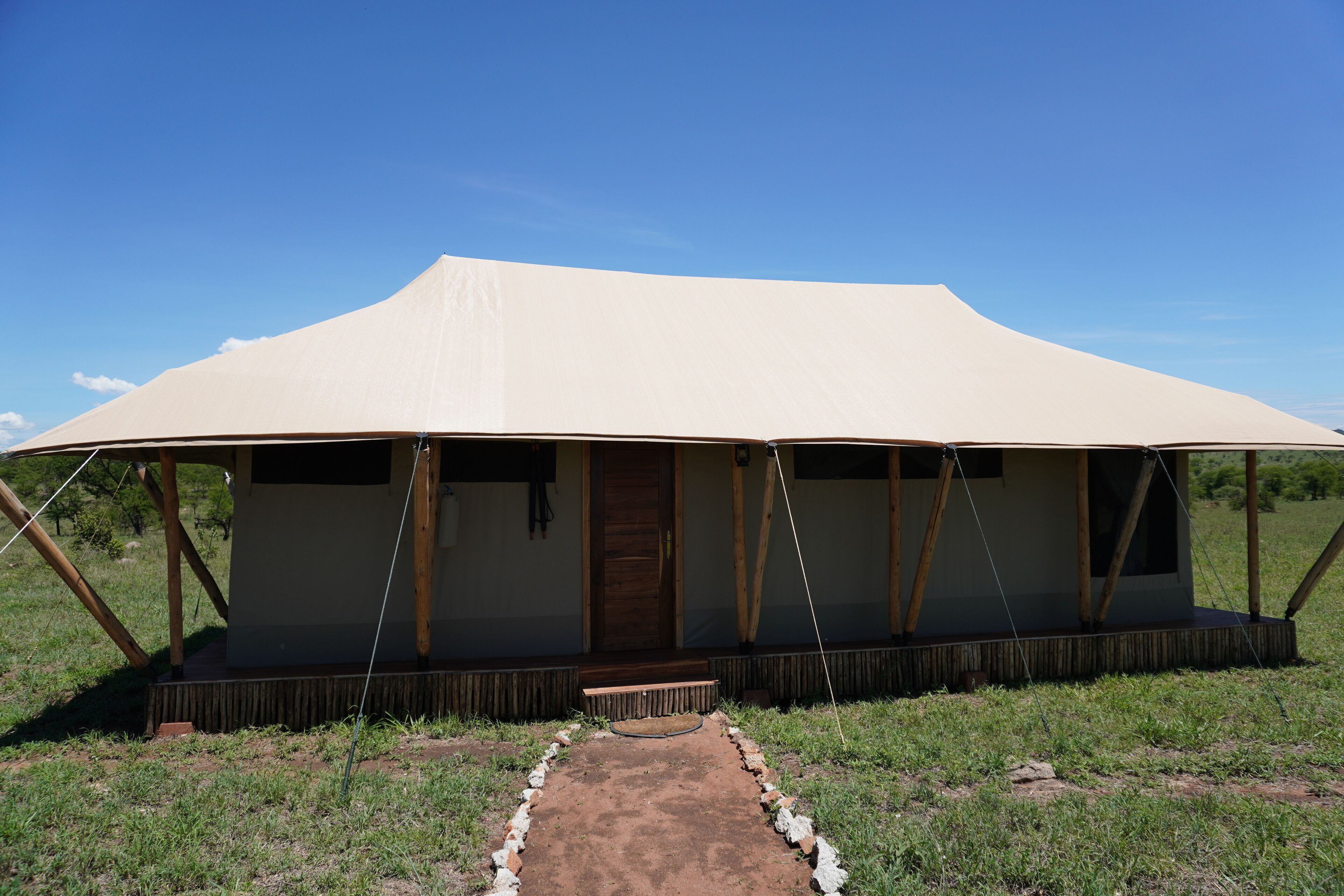 A large, open-air structure with a flat roof and a central door, surrounded by a grassy area.