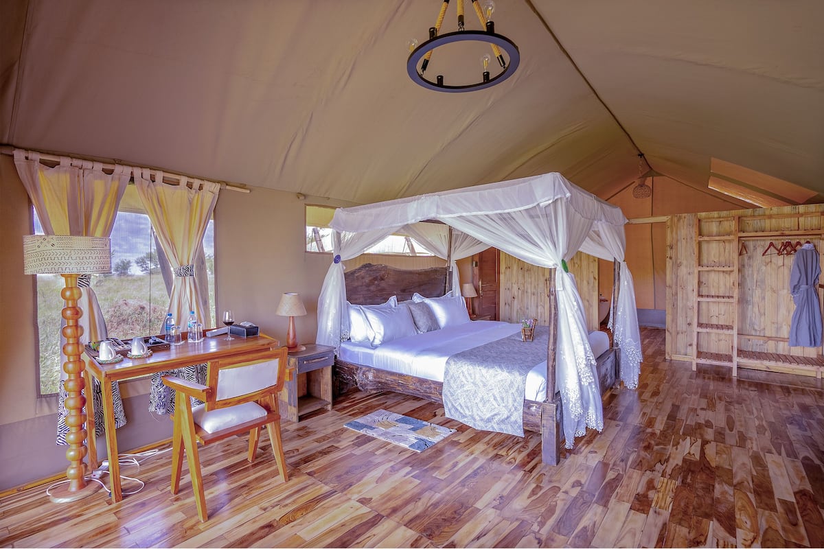 A tent-style bedroom with a canopy bed, wooden furniture, and a desk with a lamp.