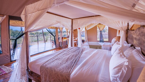 A spacious tent with a large bed, a desk, and a chair. - Malaika Luxury Camp Seronera Serengeti (Serengeti)