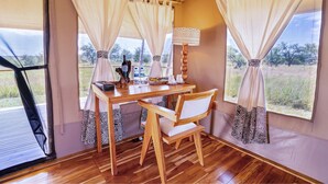 A wooden desk with a chair, curtains, and a lamp in a room with large windows. - Malaika Luxury Camp Seronera Serengeti (Serengeti)