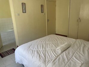 A bedroom with a bed, a door, and a bathroom visible in the background.