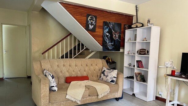 Una sala de estar con un sofá color beige, un tapete estampado, una escalera y una estantería blanca.