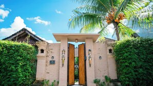 A traditional building with a wooden door, surrounded by lush greenery and a palm tree. - Gopala Villa North Ubud (Ubud)