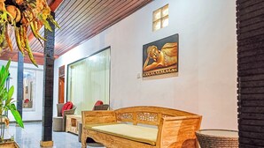 A wooden bench with a cushion, a large window, and a wall-mounted Buddha statue in a well-lit indoor space. - Gopala Villa North Ubud (Ubud)