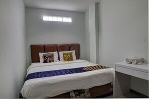 A neatly made bed with a brown headboard, white bedding, and patterned pillows. There is a small window above the bed and a white desk with towels on it. - Hotel O Finest House Near Amplas Bus Terminal (Medan)