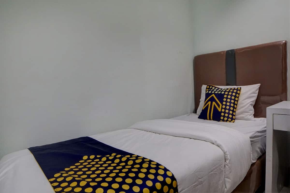 A single bed with a white mattress, a blue and yellow polka dot blanket, and a pillow with a blue and yellow pattern.