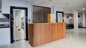 Un moderno vestíbulo de hotel con mostrador de recepción, zona de comedor y cocina visible a través de una puerta abierta.
