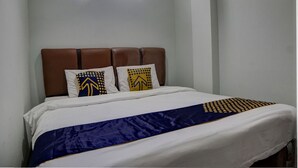 Una cama con cabecera marrón, ropa de cama blanca y almohadones decorativos.