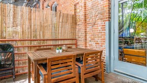 An outdoor patio with a wooden table and chairs, a bamboo fence, and a brick wall. - 100 Year-old Historic Brick 2BR Loft Large Patio2 (Durham)