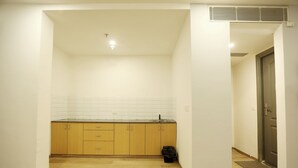 A kitchen with wooden cabinets, white tiled backsplash, and a black trash bin. - Hotel Earthview  (Noida)