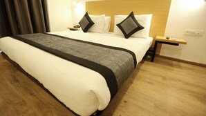 A neatly made bed with a wooden headboard, a bedside table with a lamp, and a power outlet on the wall. - Hotel Earthview  (Noida)