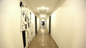 A long, narrow hallway with wooden flooring and white walls. - Hotel Earthview  (Noida)