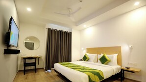 A hotel room with a bed, a desk, a television, a mirror, and a ceiling fan. - Hotel Earthview  (Noida)