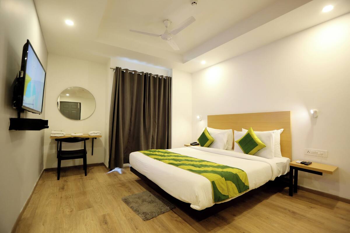 Habitación de hotel con cama, escritorio, televisor, espejo y ventilador de techo.