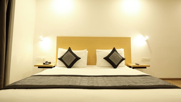 A hotel room with a large bed, two bedside tables, a wooden headboard, and two wall-mounted lights. - Hotel Earthview  (Noida)
