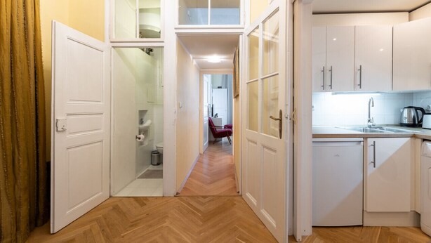 A narrow hallway with a wooden floor leading to a kitchen area with white cabinets and a refrigerator. - Historic Apartment close to Ludmila Cathedral by EasyBNB Premium (Prague)