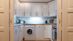 A compact kitchen with white cabinets, a washing machine, a microwave, and an oven. - Historic Apartment close to Ludmila Cathedral by EasyBNB Premium (Prague)