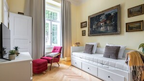 A living room with a white sofa, a red chair, a TV, and a painting on the wall. - Historic Apartment close to Ludmila Cathedral by EasyBNB Premium (Prague)
