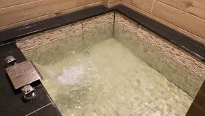 A bathtub with running water, a black faucet, and a metal control panel. - Now and Then Hot Spring Inn (Jiaoxi)