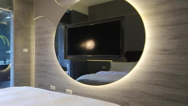 A modern bedroom with a circular mirror, a flat-screen TV, and a bed with white bedding. - Now and Then Hot Spring Inn (Jiaoxi)
