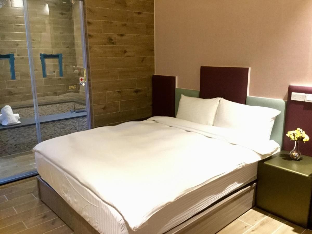 Habitación de hotel con cama, mesita de noche con un florero y puerta de vidrio que da a un balcón.