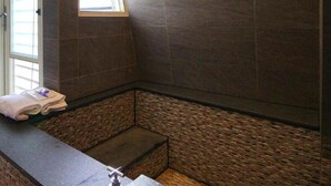 A bathroom with dark tiled walls, a window, and a small sink area. - Now and Then Hot Spring Inn (Jiaoxi)