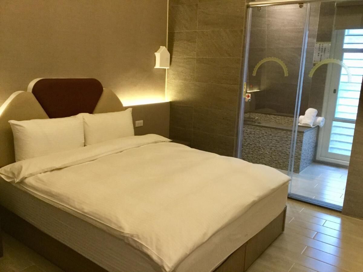 A hotel room with a bed, a shower area, and a glass door leading to a balcony.