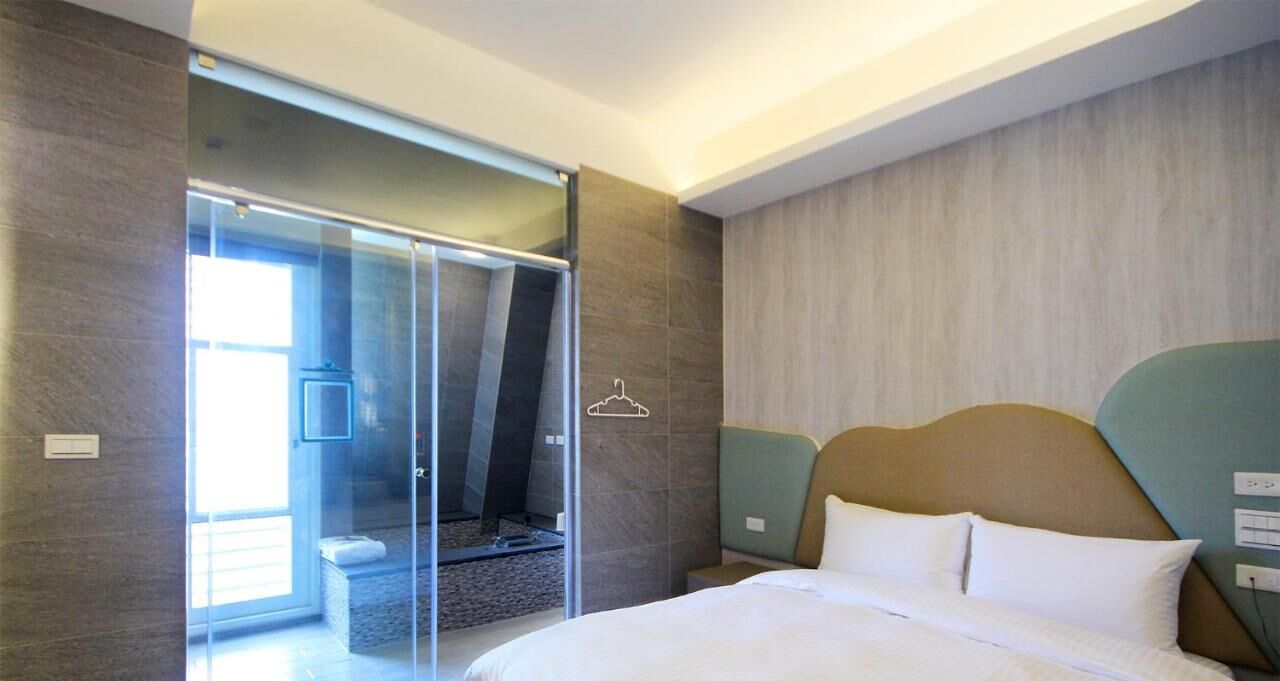 A modern hotel room with a large bed, a glass shower enclosure, and a view of the outside.