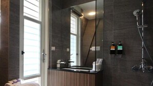 A modern bathroom with a large mirror, dark tiled walls, a shower, and a sink with a towel on the counter. - Now and Then Hot Spring Inn (Jiaoxi)