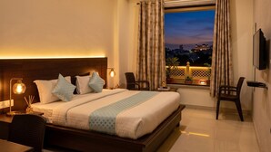 A hotel room with a bed, bedside table, lamp, chair, TV, and a balcony with a view. - Jeenmount Heritage Boutique Hotel-JLN Marg (Jaipur)