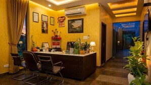 A reception area with a desk, chairs, potted plants, framed certificates, and an air conditioning unit. - Jeenmount Heritage Boutique Hotel-JLN Marg (Jaipur)