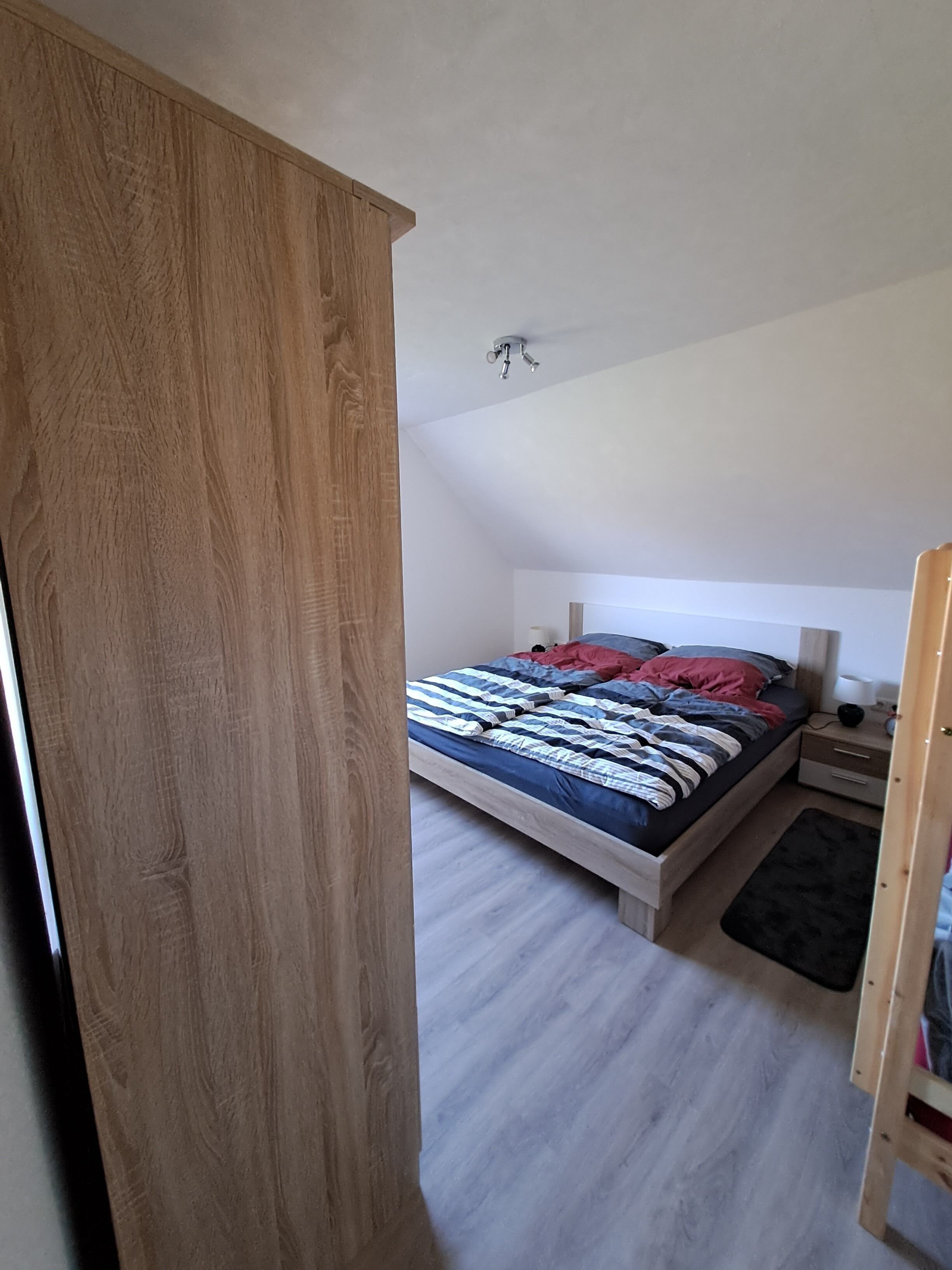 Un dormitorio con una cama, una mesita de noche, un armario de madera y una lámpara en el techo.
