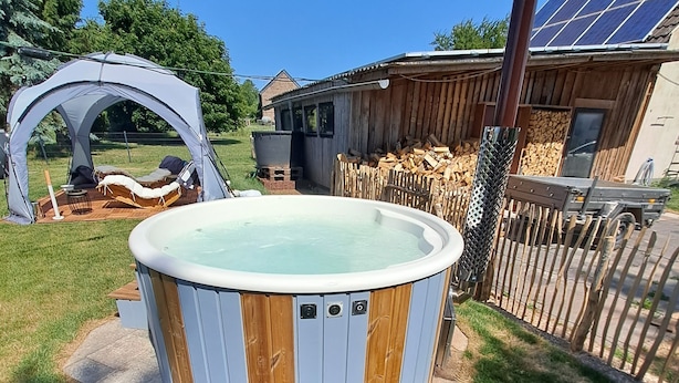 A hot tub in a backyard with a wooden deck, a tent, and a solar panel. - Gemütliche Wohnung im Nationalpark Eifel mit Outdoor Wellnessbereich (Mechernich)