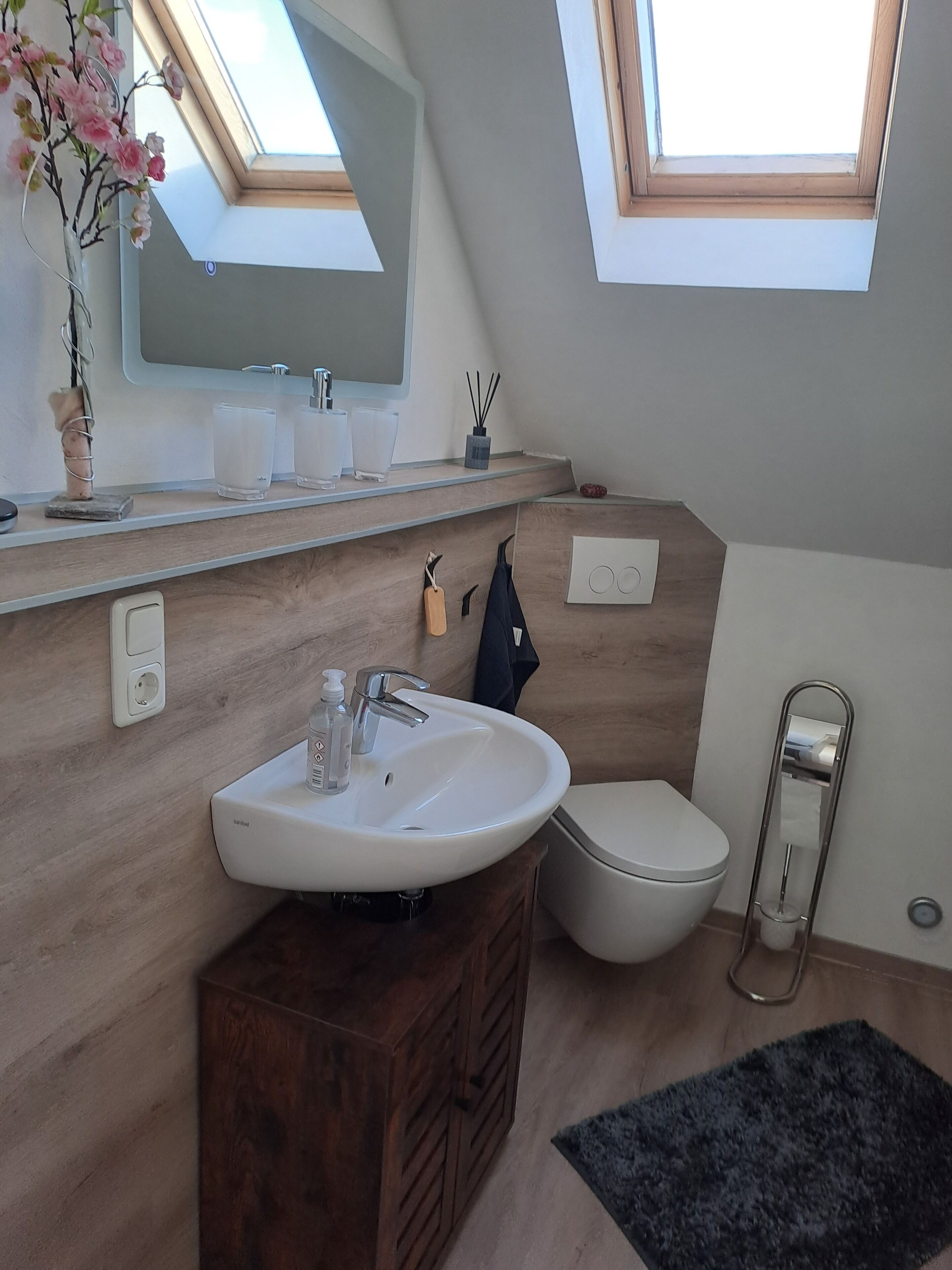 Un baño moderno con tragaluz, tocador de madera, lavamanos blanco y inodoro.