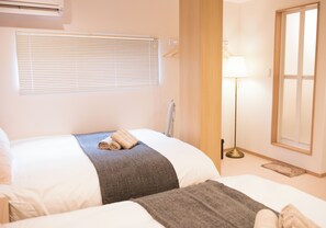 Habitación de hotel con dos camas, un calentador portátil, una mesita de noche, una lámpara y una ventana con persianas.