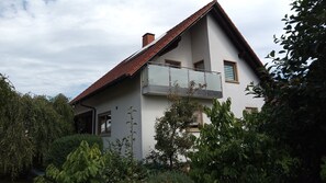 Ein zweistöckiges Haus mit Balkon, umgeben von viel Grün.