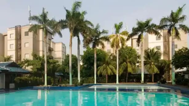 A swimming pool with clear blue water, surrounded by palm trees and modern buildings. - D'Arcici Hotel Sunter (Jakarta)