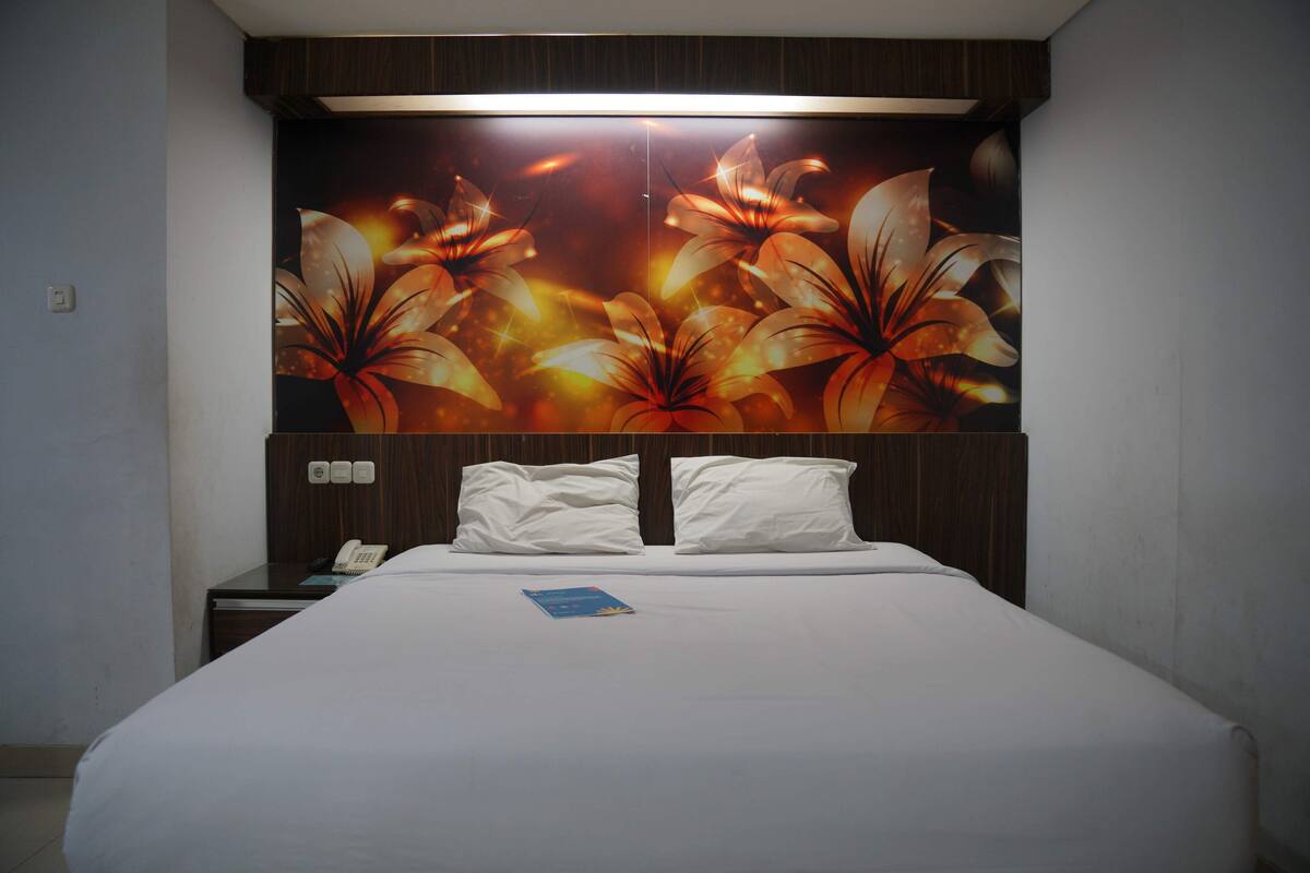 Habitación de hotel con una cama grande, ropa de cama blanca, una mesita de noche con teléfono y una pared con un mural floral.