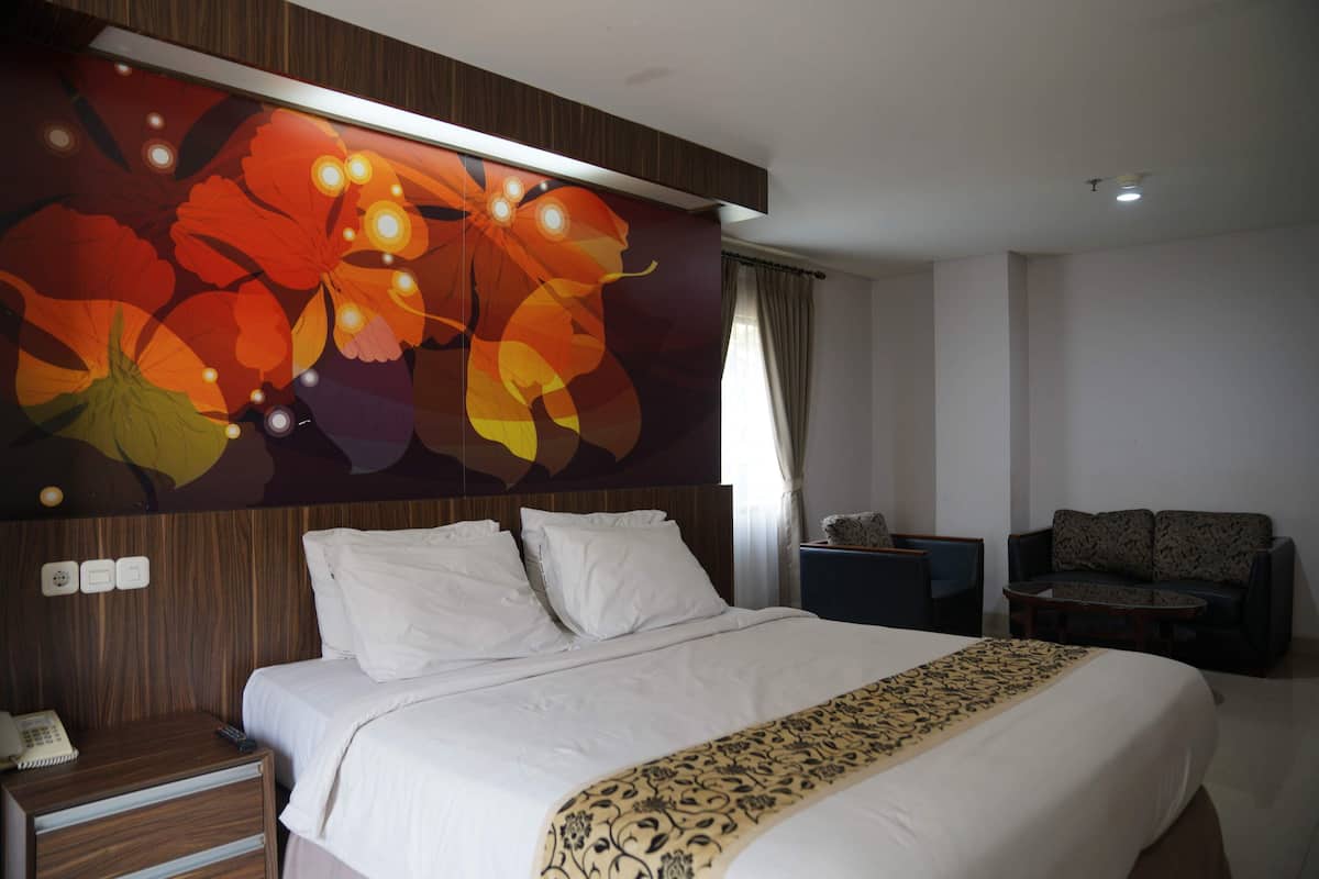 Una habitación de hotel con una cama grande, una mesita de noche con un teléfono y una lámpara, un sofá y una pared con un mural floral.