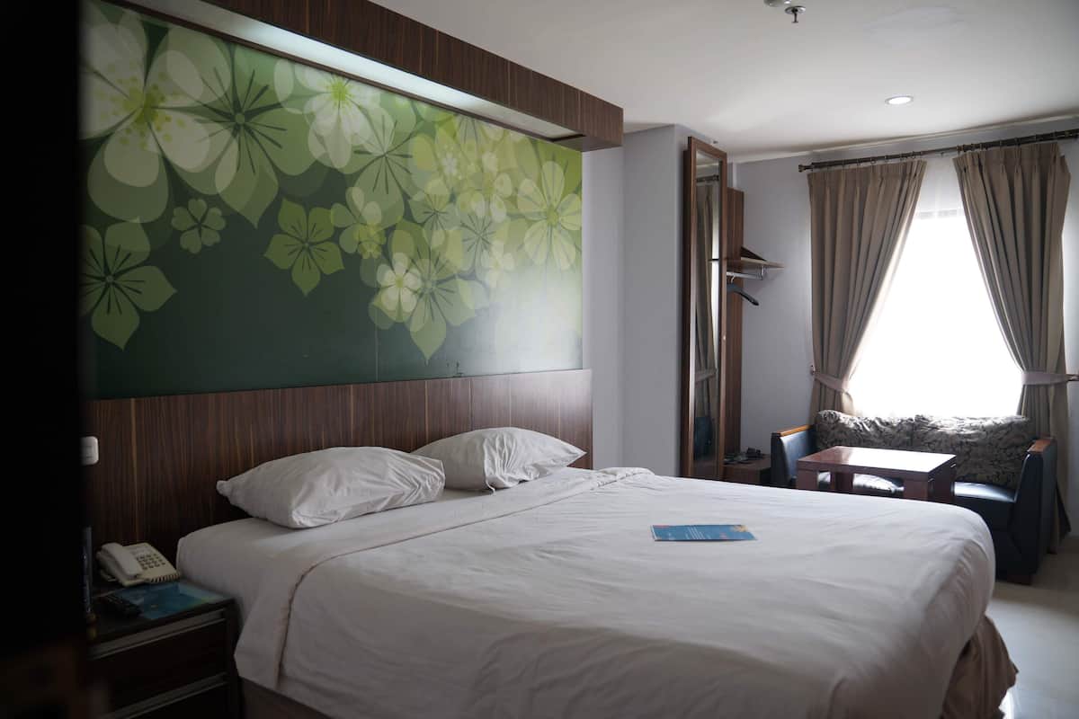 Habitación de hotel con una cama grande, una mesita de noche con teléfono y control remoto, una pequeña mesa y un mural floral grande en la pared.