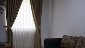 A living room with a glass coffee table, a dark sofa, and beige curtains. - D'Arcici Hotel Sunter (Jakarta)