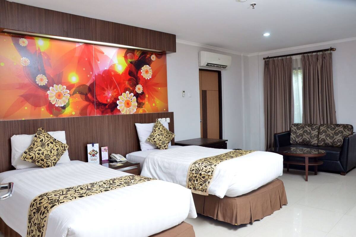 Habitación de hotel con dos camas, un sofá, una mesita de centro y una gran obra de arte floral en la pared.