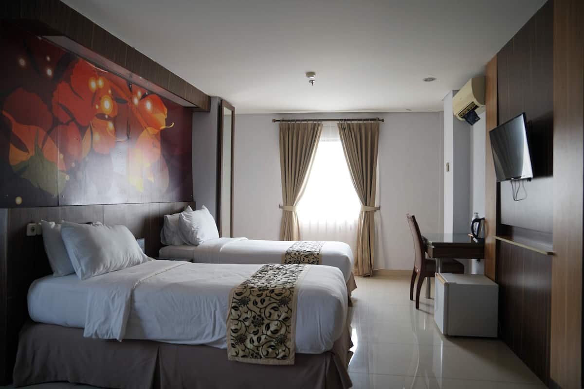 Habitación de hotel con dos camas, un escritorio, una silla, un televisor y un ventanal con cortinas.