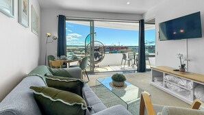 Una sala de estar moderna con sofá, mesa de centro y televisor. Hay un balcón con vistas a la ciudad y una silla colgante.