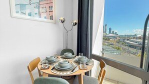 Un comedor con una mesa redonda dispuesta para cuatro personas, vista a la ciudad a través de amplias ventanas y un cuadro en la pared.